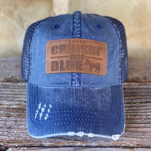 May include: A blue denim trucker hat with a brown leather patch that says "Cruisin' 2020 Blue" with a donkey silhouette.