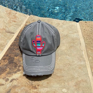 May include: A gray distressed baseball cap with a colorful embroidered cactus design. The cactus is red, orange, yellow, green, blue, and purple.
