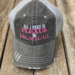 May include: A black and gray distressed baseball cap with a white mesh back. The cap has the text "All I need is Plexus & Mascara" embroidered on the front in pink and white.