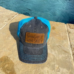 May include: A black and blue trucker hat with a brown leather patch that says "Sunshine & Whiskey".