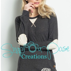 May include: A charcoal gray long-sleeved shirt with white elbow patches and a white monogram on the front. The shirt has a relaxed fit and features a button detail on the side.
