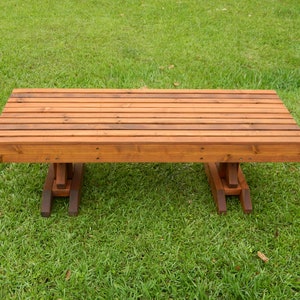 May include: A wooden bench with a natural brown finish. The bench has a slatted top and simple, sturdy legs.