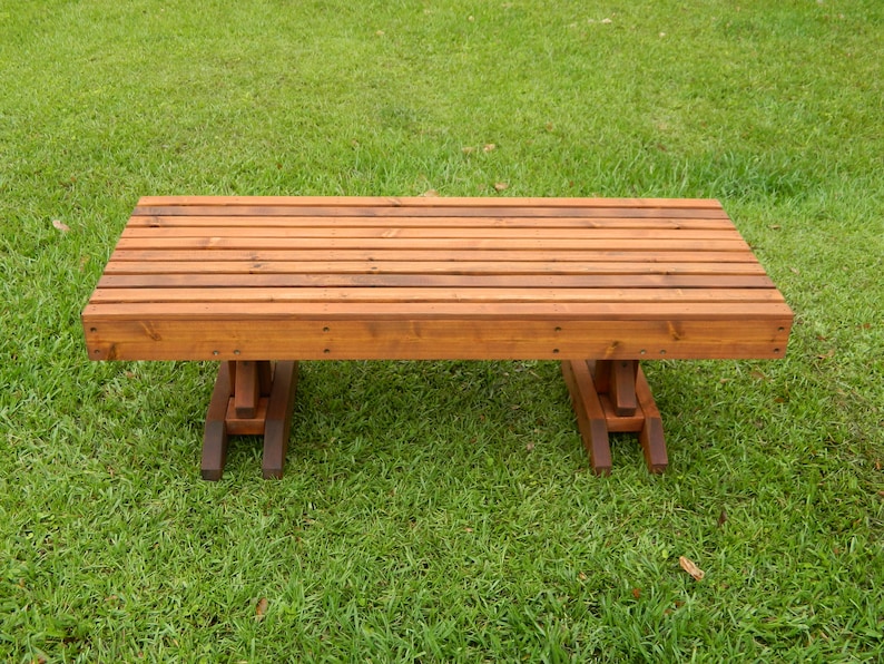 May include: A wooden bench with a natural brown finish. The bench has a slatted top and simple, sturdy legs.