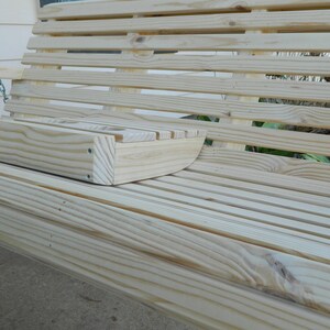 May include: A wooden swing with a built-in cup holder. The swing is made of natural wood and has a slatted design. The cup holder is located on the right side of the swing.