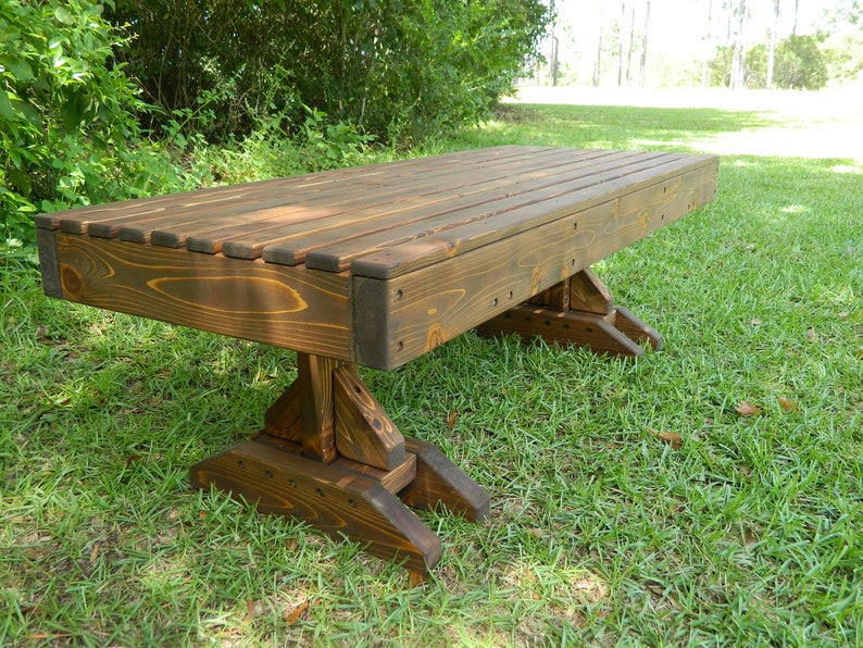 May include: A dark brown wooden bench with a slatted top and a unique, sturdy base. The bench is sitting on a grassy lawn.