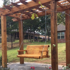 K&ouml;nnte beinhalten: Eine h&ouml;lzerne Schaukelbank h&auml;ngt an einer Pergola aus Zedernholz. Die Schaukel ist an zwei Ketten aufgeh&auml;ngt und befindet sich in einem Garten.