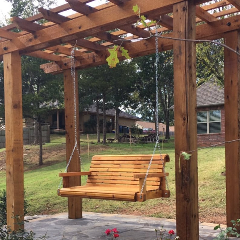 K&ouml;nnte beinhalten: Eine h&ouml;lzerne Schaukelbank h&auml;ngt an einer Pergola aus Zedernholz. Die Schaukel ist an zwei Ketten aufgeh&auml;ngt und befindet sich in einem Garten.