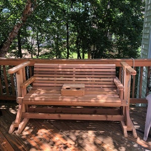May include: A wooden swing bench with a cup holder, made of cedar wood, on a wooden deck.