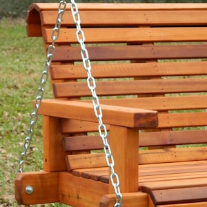 Puede incluir: Un banco de columpio de madera con un acabado de madera natural. El columpio est&aacute; suspendido por dos cadenas plateadas.