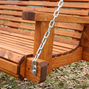 May include: Close-up of a wooden swing set with a brown stain finish. The swing is made of sturdy wood and has a metal chain hanging from it. The swing is set against a backdrop of brown leaves.