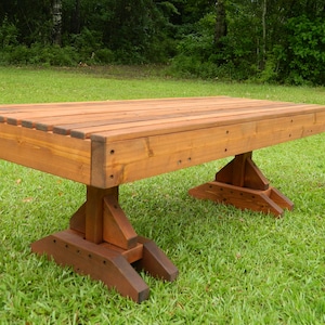 May include: A long, wooden bench with a natural brown stain. The bench has a simple, rectangular design with a flat top and four legs. The bench is made of solid wood and has a rustic look.