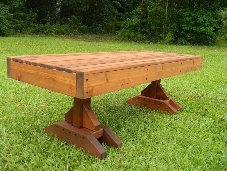 May include: A long, wooden bench with a natural brown stain. The bench has a simple, rectangular design with a flat top and four legs. The bench is made of solid wood and has a rustic look.