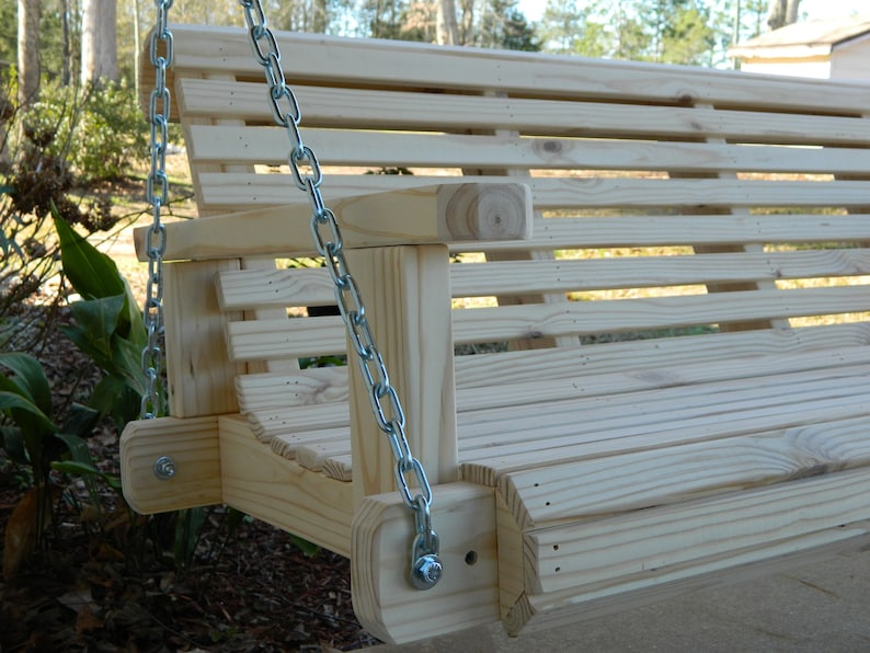 May include: A wooden porch swing with slatted back and seat, hanging from two silver chains. The swing is made of unfinished wood and has a simple design.