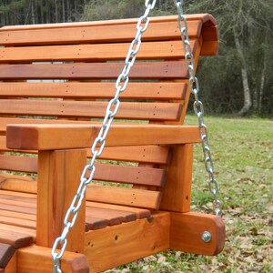 Puede incluir: Un columpio de madera con un acabado de cedro natural y cadenas plateadas. El columpio est&aacute; hecho de listones y tiene un respaldo redondeado.