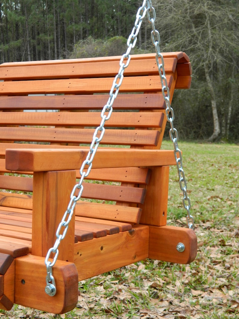 Puede incluir: Un columpio de madera con un acabado de cedro natural y cadenas plateadas. El columpio est&aacute; hecho de listones y tiene un respaldo redondeado.