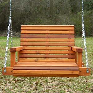 Puede incluir: Un columpio de madera con respaldo y asiento de listones. El columpio est&aacute; colgado de dos cadenas y est&aacute; suspendido en el aire. El columpio est&aacute; hecho de madera natural y tiene un aspecto r&uacute;stico.