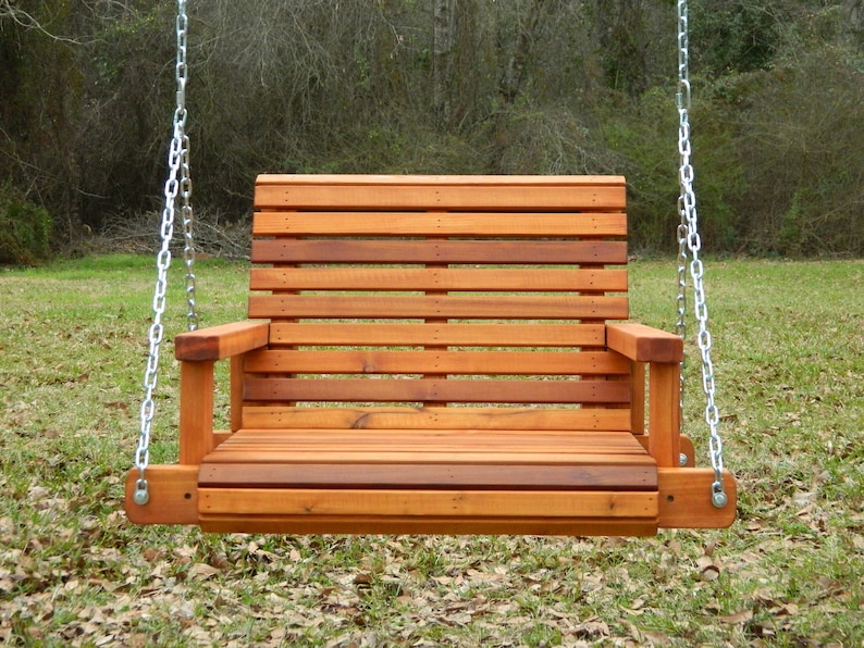 Puede incluir: Un columpio de madera con respaldo y asiento de listones. El columpio est&aacute; colgado de dos cadenas y est&aacute; suspendido en el aire. El columpio est&aacute; hecho de madera natural y tiene un aspecto r&uacute;stico.