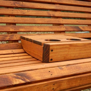 May include: A wooden bench with a built-in cup holder. The cup holder is made of the same wood as the bench and has two slots for cups. The bench is stained a dark brown color.