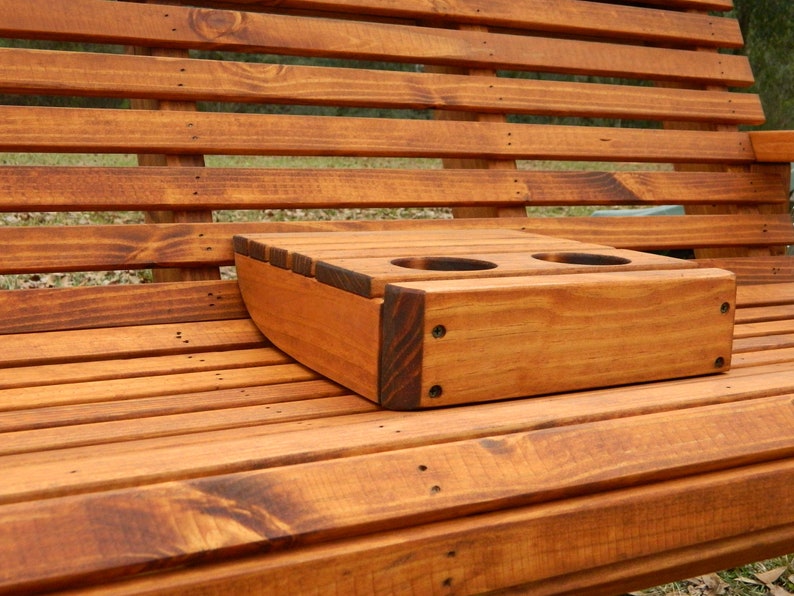 May include: A wooden bench with a built-in cup holder. The cup holder is made of the same wood as the bench and has two slots for cups. The bench is stained a dark brown color.