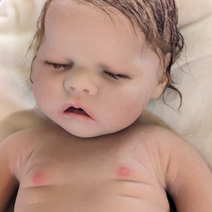 May include: A realistic baby doll with closed eyes and wet brown hair. The doll is made of silicone and has a lifelike appearance.