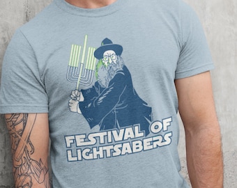 May include: A light blue t-shirt with a graphic of a man holding a lightsaber, with the text "Festival of Lightsabers".