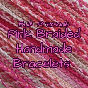 Puede incluir: Primer plano de pulseras rosas trenzadas hechas a mano. Las pulseras están hechas de varios tonos de rosa, blanco y melocotón. El texto "Bulk Premade Pink Braided Handmade Bracelets" se muestra en fuente rosa.