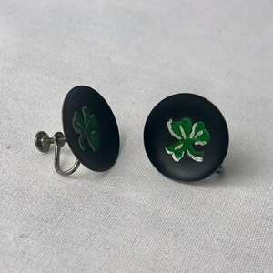 May include: A pair of black and green clover-shaped earrings with silver screw-back closures.