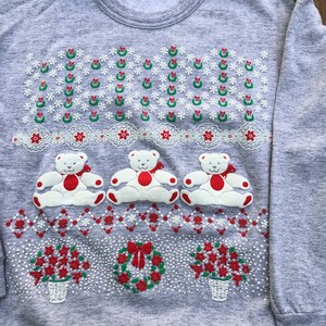 May include: A gray sweatshirt with a Christmas design featuring three white teddy bears, wreaths, and poinsettia flowers. The sweatshirt has the text "Aspirations" on the tag.