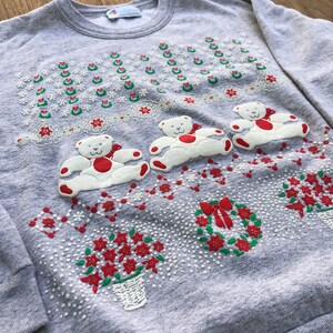 May include: Gray Christmas sweater with a white, green, and red embroidered design of teddy bears, wreaths, and poinsettias.