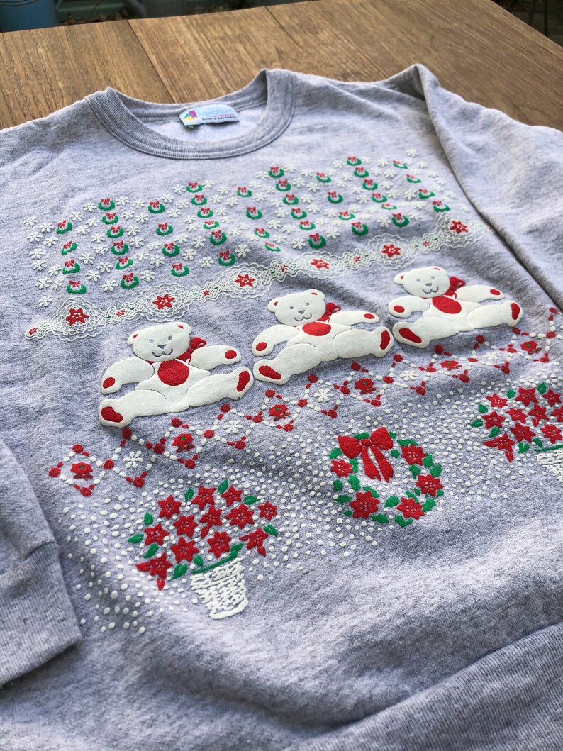 May include: Gray Christmas sweater with a white, green, and red embroidered design of teddy bears, wreaths, and poinsettias.