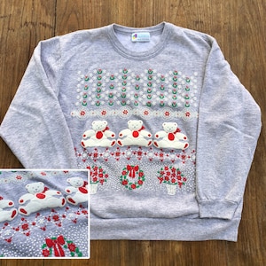 May include: Gray Christmas sweatshirt with a festive design featuring three white teddy bears wearing red bows, wreaths, and poinsettia flowers. The text "Holiday" is printed on the tag.