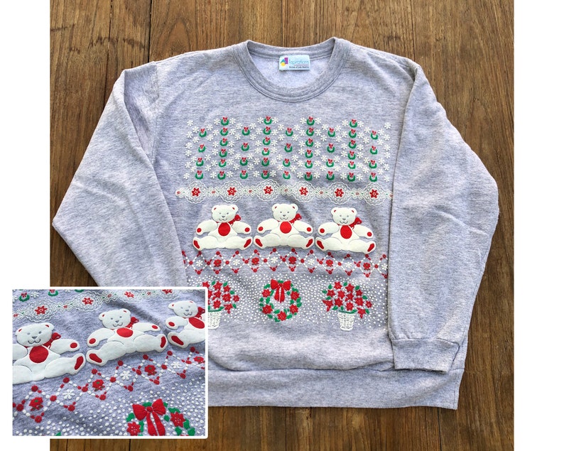 May include: Gray Christmas sweatshirt with a festive design featuring three white teddy bears wearing red bows, wreaths, and poinsettia flowers. The text "Holiday" is printed on the tag.