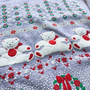 May include: Gray Christmas sweater with a white teddy bear design. The sweater has a red and green wreath pattern with a red bow.