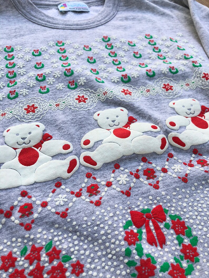 May include: Gray Christmas sweater with a white teddy bear design. The sweater has a red and green wreath pattern with a red bow.