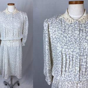 Puede incluir: Un vestido blanco con estampado de mariposas blancas y grises. El vestido tiene un cuello de encaje y mangas largas.