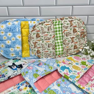 May include: A collection of quilted oven mitts and pot holders with various patterns. Designs include daisies, bunnies with carrots, and Easter eggs. Colors include blue, yellow, green, and pink. The mitts and holders are made of fabric.