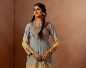 May include: A woman wearing a light blue and yellow ombre kurta with intricate embroidery. The kurta has a V-neckline and long sleeves. She is also wearing matching pants and a dupatta.