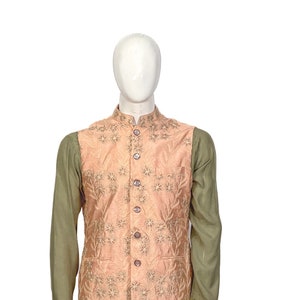 Op de afbeelding: Een perzikkleurig vest met bloemenborduursel, gedragen over een lang mouwig groen shirt en een bijpassende broek.