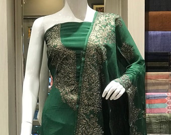 May include: A deep green sleeveless dress featuring intricate silver-toned embroidery along the neckline and down the front panel. The garment is draped over a white mannequin, showcasing a long, flowing silhouette with a matching shawl draped over one shoulder.