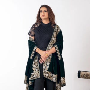 Op de afbeelding: Een persoon draagt een zwarte kanten top en zwarte broek, bedekt met een donkergroene fluwelen sjaal. De sjaal is versierd met ingewikkelde gouden en crèmekleurige bloemenborduursels. De outfit staat tegen een witte achtergrond.