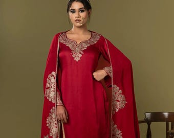 May include: A deep red silk-like tunic and trousers set featuring intricate gold embroidery along the neckline, sleeve cuffs, and pant hems. A matching red shawl with large gold floral patterns is draped over the shoulders, paired with a gold drawstring pouch.