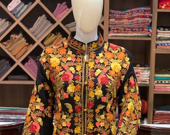 May include: A black long-sleeved coat featuring a high collar and a front button closure. The garment is decorated with dense, colorful floral embroidery in shades of red, orange, yellow, and green, covering the entire front and sleeves.