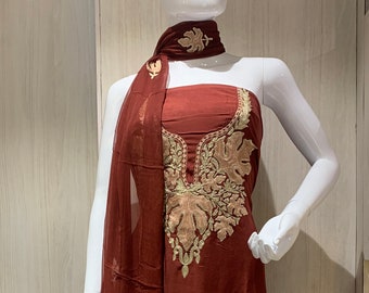 May include: A dark rust-coloured sleeveless dress featuring intricate beige floral embroidery around the neckline. The garment is paired with a matching sheer, lightweight scarf draped over the shoulder, which also displays delicate beige floral embroidery.
