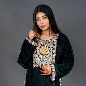 May include: A dark green velvet tunic featuring a prominent rectangular chest panel with gold leaf embroidery and intricate floral needlework. The garment includes long sleeves with matching floral borders at the cuffs and hemline, plus side slits.