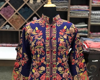 May include: A long-sleeved navy blue coat featuring a mandarin collar and a front button closure. The garment is decorated with intricate, multi-colored floral and paisley embroidery in shades of orange, pink, green, and yellow throughout the fabric.