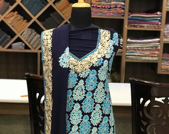 May include: A dark navy blue sleeveless tunic and matching shawl featuring intricate embroidery in light blue and cream. The garment displays a repeating paisley pattern across the front, with a V-neckline and a wide decorative border along the hem.