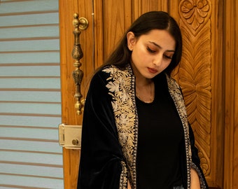 May include: A navy blue velvet shawl with intricate gold embroidery. The shawl is draped over a person's shoulders and has a flowing design.
