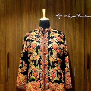 May include: Black jacket with detailed floral embroidery in orange, red, and green. It has a mandarin collar and a button-down front. The sleeves and hem are also decorated with patterns. The text "4 Angad Creations" is visible.