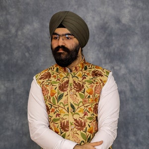 Peut inclure: Un homme portant une chemise blanche, un gilet &agrave; motifs floraux et un turban vert. Il porte une montre au poignet gauche.