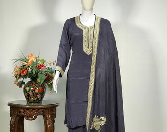 May include: A gray and gold embroidered kurta and palazzo set with a matching dupatta. The kurta has a round neckline and long sleeves. The palazzo pants are wide-legged and the dupatta is sheer with a floral design.